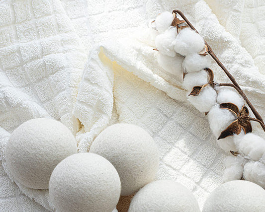 Five wool dryer balls on top of a towel and a branch of cotton plant in the background.